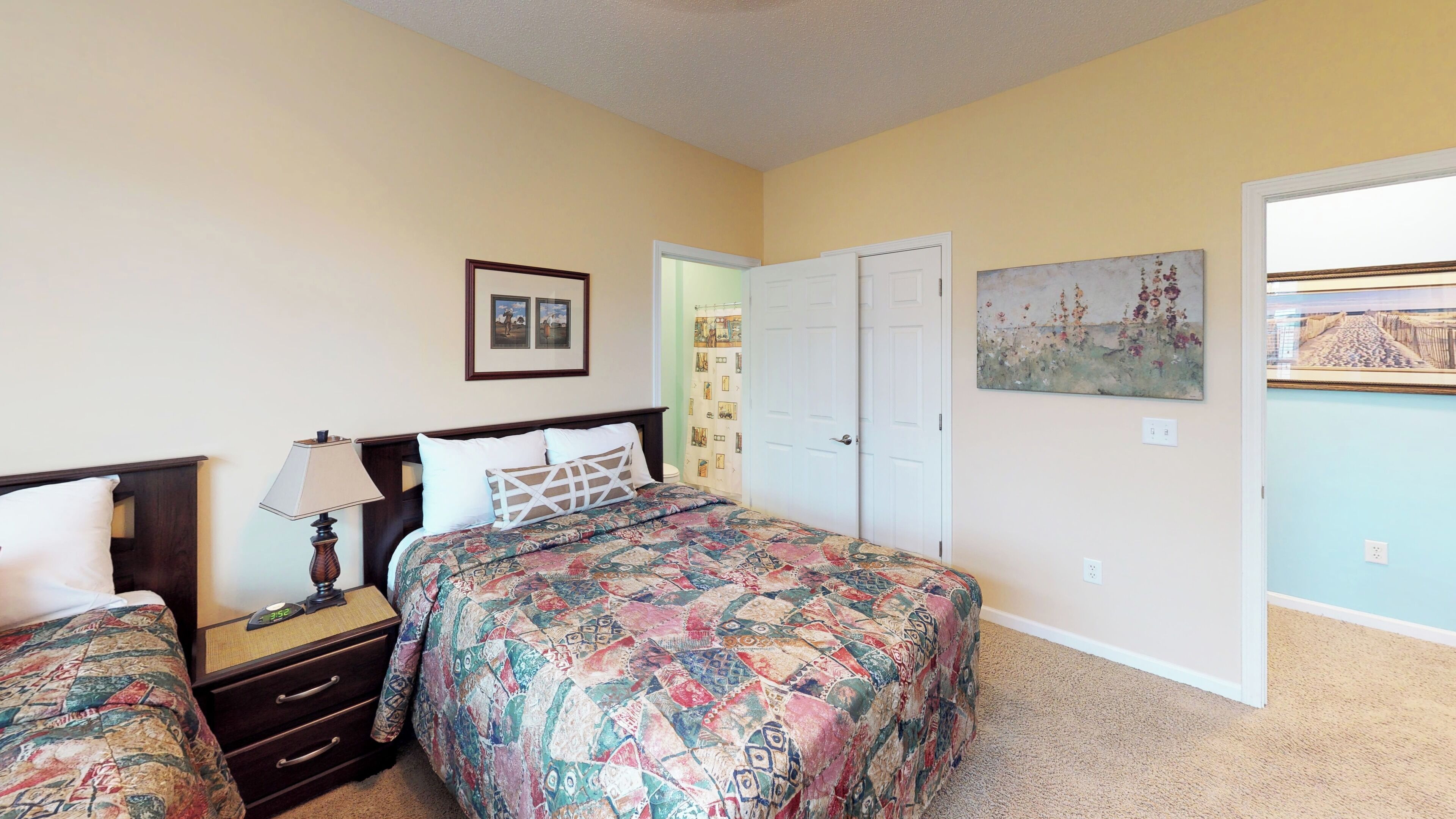 A bedroom with two beds, a nightstand, a lamp, a door, and a painting on the wall.