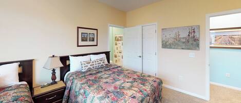 A bedroom with two beds, a nightstand, a lamp, a door, and a painting on the wall.