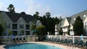 A swimming pool with a curved edge, surrounded by lounge chairs and a white fence. - Village at the Glens S 205 (Little River)