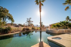 Une piscine aux eaux cristallines, avec un palmier au centre, entourée d’une clôture et de différentes plantes.
