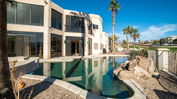 Une maison moderne à deux étages, dotée d’une piscine, de palmiers et surplombant un ciel d’un bleu limpide.