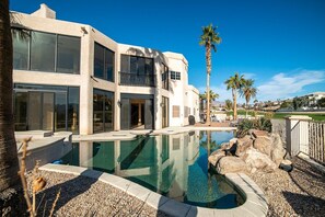 A modern two-story house with a swimming pool, palm trees, and a clear blue sky. - Luxury Golf Course Retreat on Hogan (Lake Havasu City)