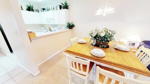A dining area with a wooden table set for four, white chairs, and a potted plant centerpiece. - Village at the Glens K 102 (Little River)