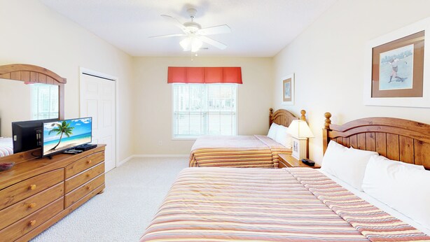 A bedroom with two beds, a TV on a dresser, a ceiling fan, and a window with blinds. - Village at the Glens K 102 (Little River)