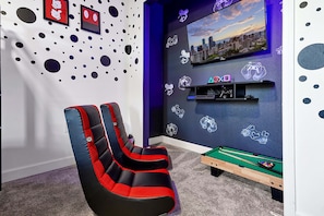 Een kamer met een pooltafel, game stoelen, een televisie en uitzicht op de stad.