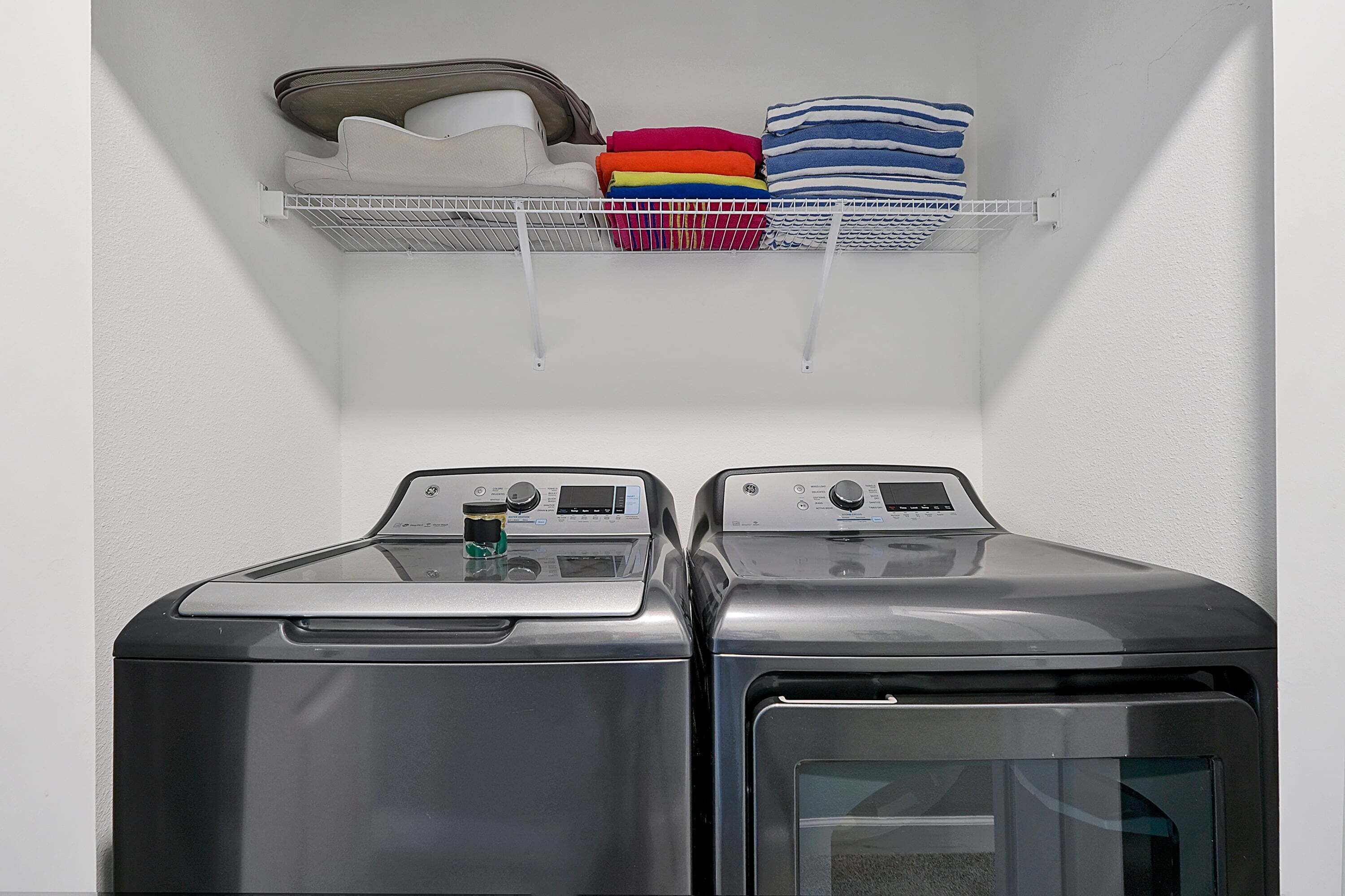 Un espace buanderie comprenant deux machines à laver à chargement frontal et une étagère métallique au-dessus, où sont pliées les serviettes, ainsi qu'un porte-chaussures.