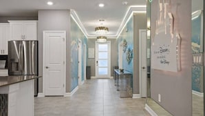 A modern kitchen with a stainless steel refrigerator, a hallway with a chandelier, and a Disney-themed wall. - Top Luxury Villa Storey Lake Mins to Disney (Kissimmee)