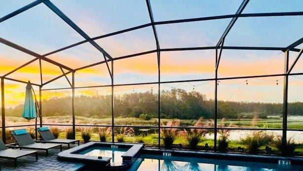 An indoor swimming pool with a glass ceiling, lounge chairs, and a view of a lake and trees. - Top Luxury Villa Storey Lake Mins to Disney (Kissimmee)