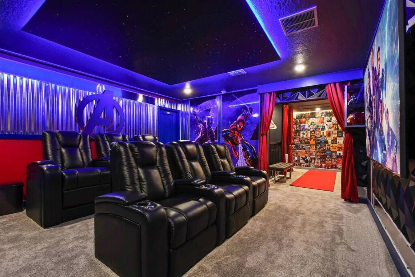 Ein Heimkinozimmer mit Ledersesseln, einem roten Teppich und einer Wand, die mit Filmplakaten dekoriert ist.