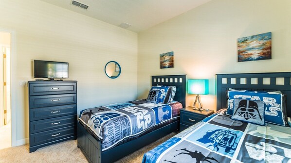 Quarto com duas camas, penteadeira, televisão e luminária fixada na parede.