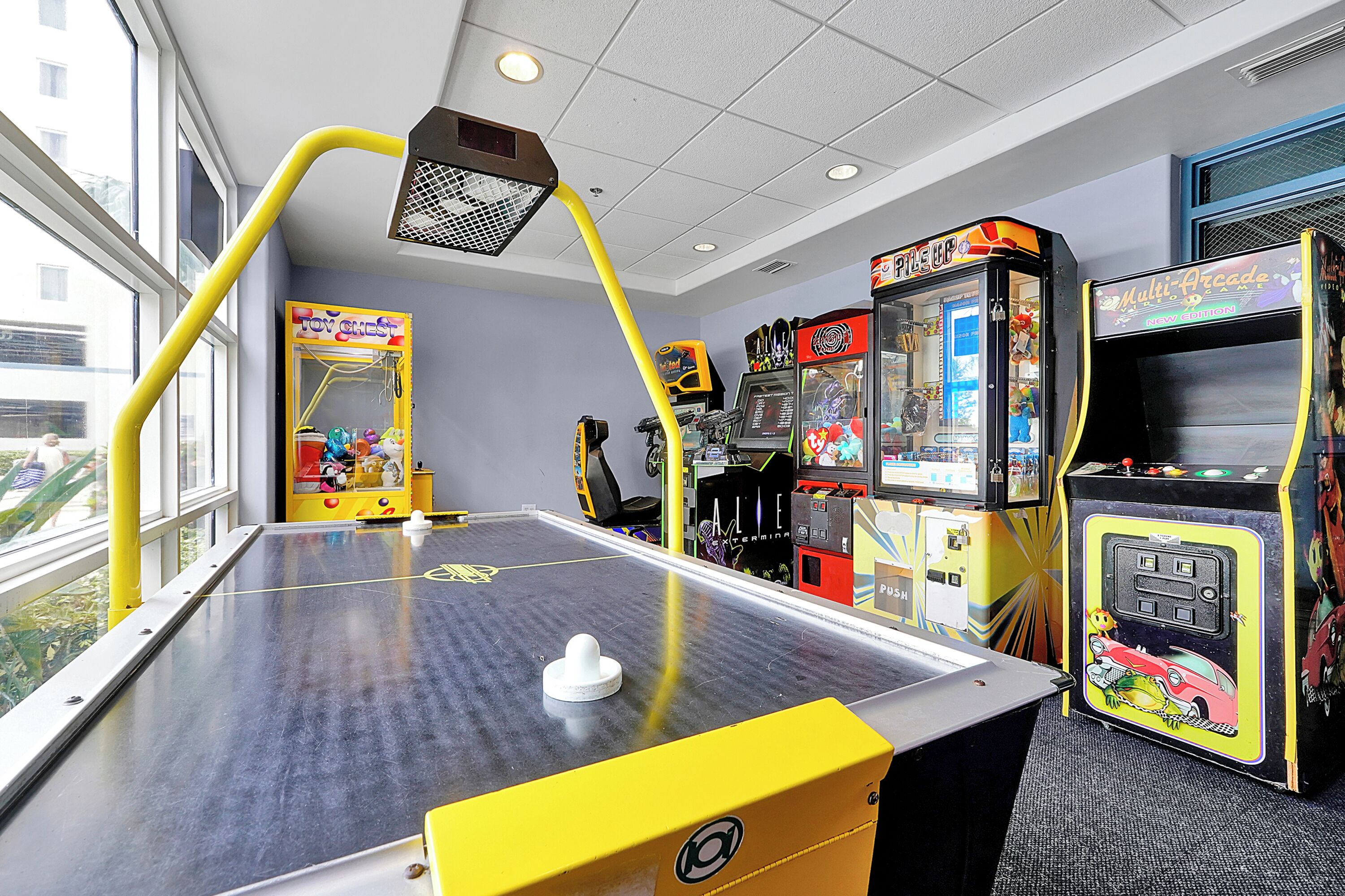 A room with a pool table, arcade games, and a window providing a view of the outside.