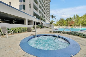 Ein Bereich mit Whirlpool, Pool, Außenmöbeln und einem Gebäude mit mehreren Etagen und Balkonen.
