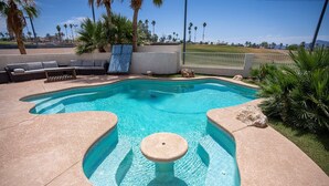 Una piscina de forma singular, rodeada por una terraza de piedra y palmeras.