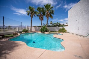 Une piscine au design incurvé, entourée d’une terrasse en béton et de palmiers.