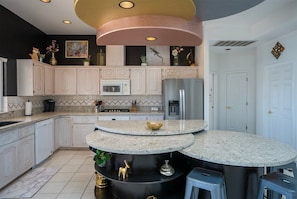 Una cocina moderna con una isla central, muebles blancos, electrodomésticos de acero inoxidable y detalles decorativos.