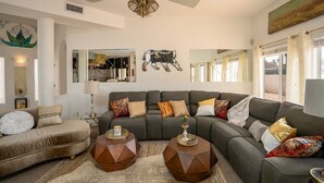 Una sala moderna con un sofá modular, dos mesas auxiliares hexagonales, un ventilador de techo y un espejo grande.