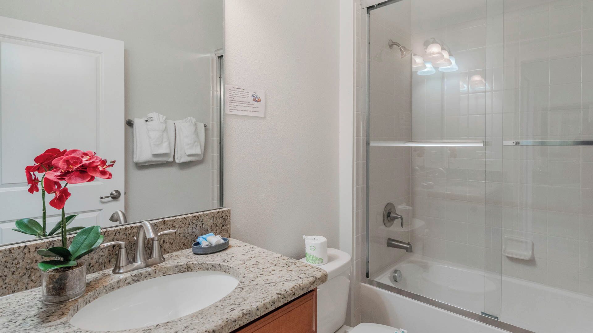 A bathroom with a granite countertop sink, a glass shower enclosure, and a white toilet.