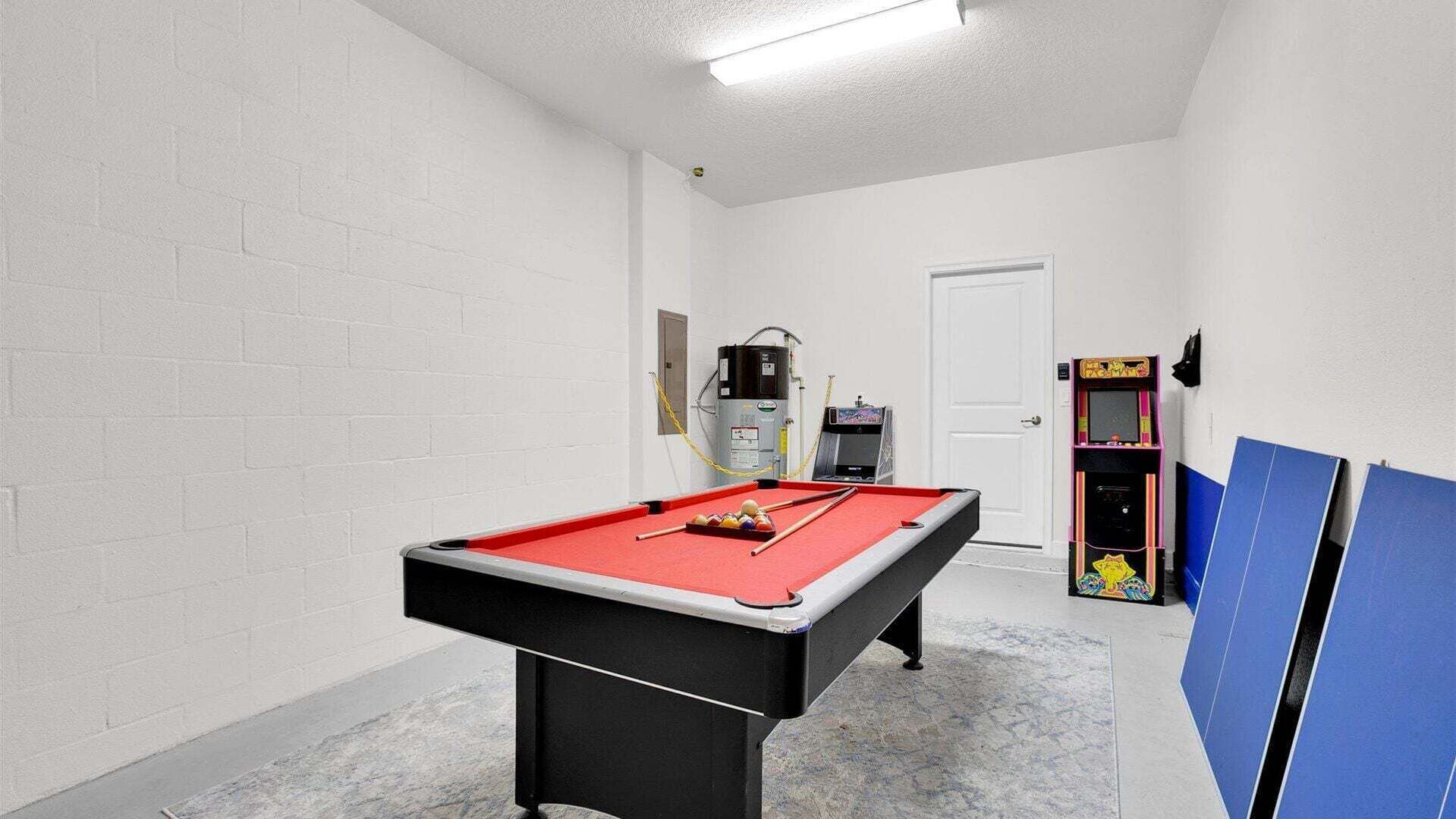 A pool table with balls, a water heater, and a pinball machine in a room with white brick walls and a door.