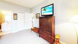 A room with a television on a wooden cabinet, a white door, and a small table with a lamp. - Village at the Glens C 204 (Little River)
