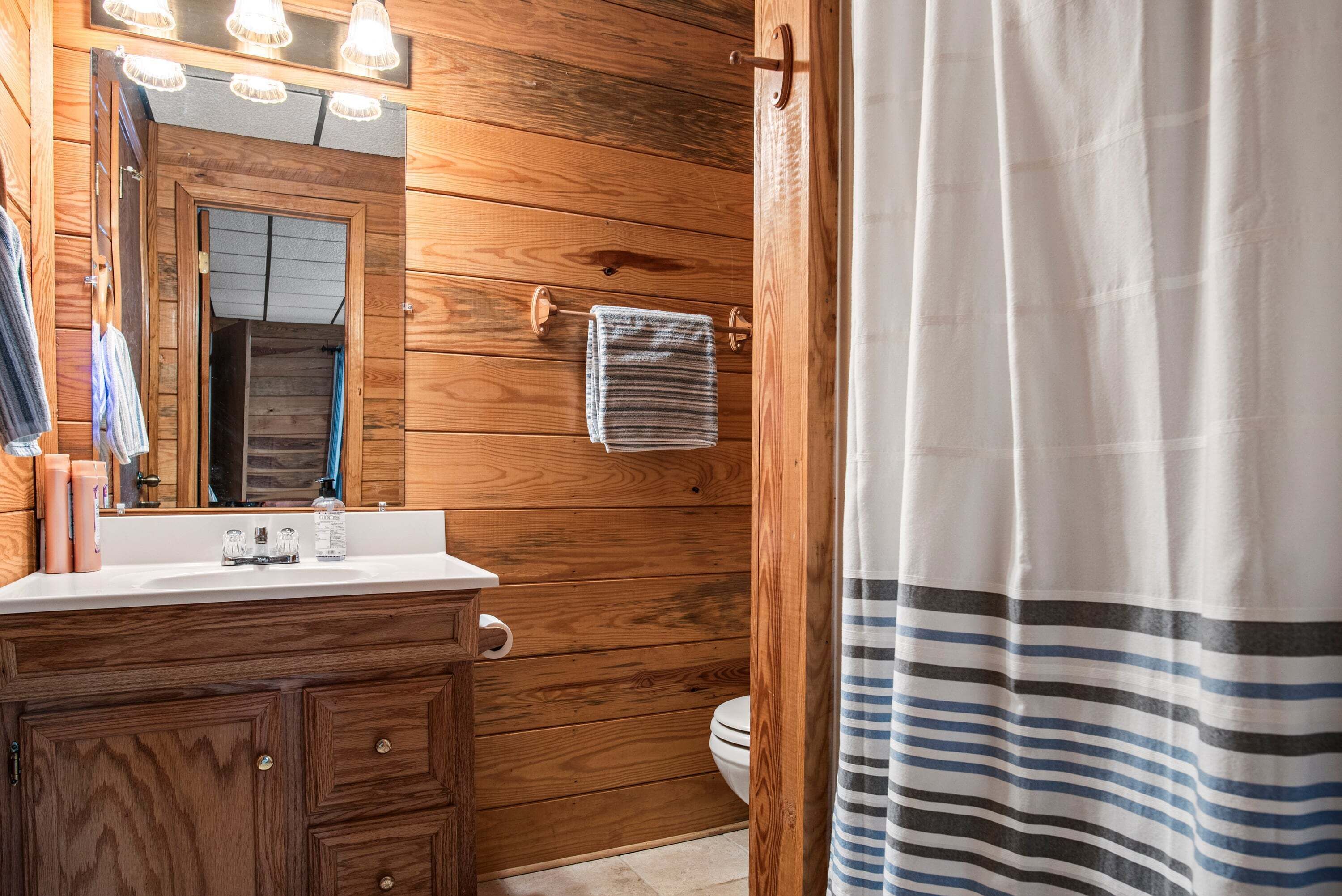 Un baño con paneles de madera, un tocador, un espejo, un perchero para toallas y una cortina de ducha a rayas.