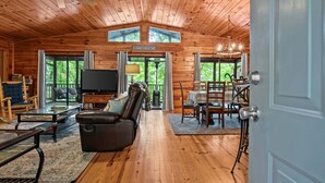 A log cabin interior with a television, leather sofa, dining table, and a sign reading 'LAKE HOUSE.' - Dogwood Cabin (Martin)