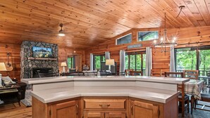 A cabin interior with a stone fireplace, wooden ceiling, and a dining area with a view of the outdoors. - Dogwood Cabin (Martin)