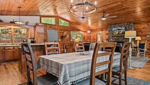 A wooden cabin interior with a dining table, chairs, a chandelier, a fireplace, and a stone wall. - Dogwood Cabin (Martin)