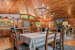 A wooden cabin interior with a dining table, chairs, a chandelier, a fireplace, and a stone wall. - Dogwood Cabin (Martin)