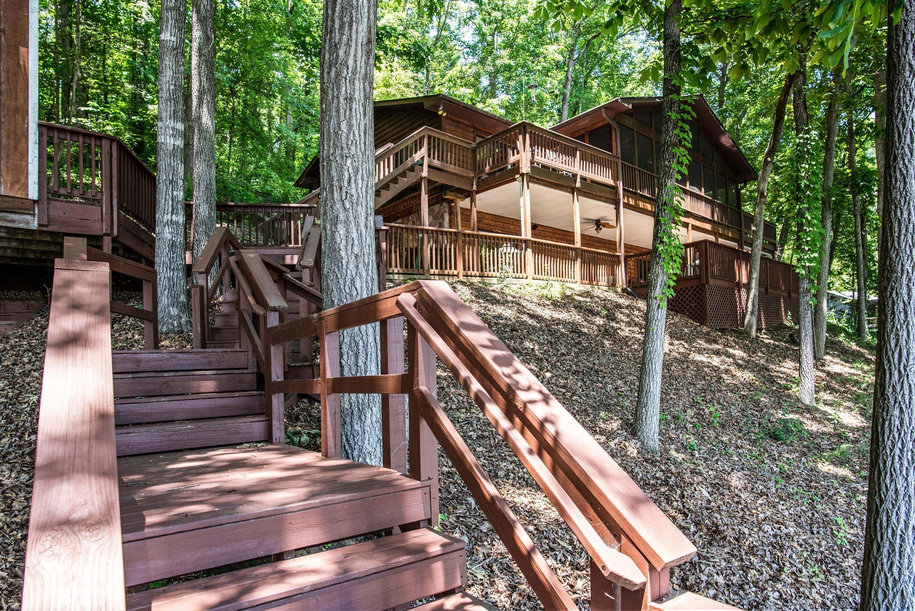 A wooden cabin with a staircase leading to a deck, surrounded by trees.