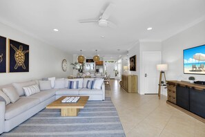 A modern living room with a sectional sofa, a coffee table, and a TV. There is a kitchen in the background with a dining area. - Waterfront Luxury Villa 35 With Boat Slip and Sunset Views (Marathon)