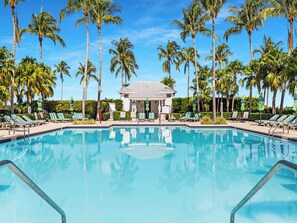 A swimming pool surrounded by lounge chairs and palm trees, with a building in the background. - Waterfront Luxury Villa 35 With Boat Slip and Sunset Views (Marathon)
