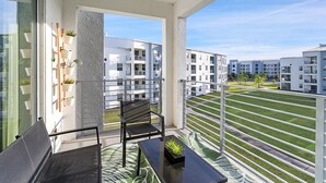 Een balkon met een zwarte stoel, een tafeltje en een potplant.
