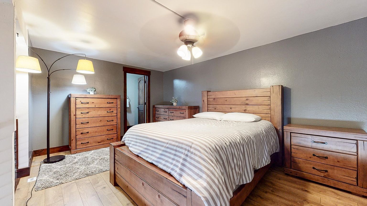 A bedroom with a wooden bed, two nightstands, a floor lamp, and a ceiling fan.