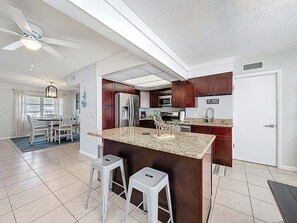 A modern kitchen with a central island, stainless steel appliances, and a dining area with a ceiling fan. - Largo Pool House and Firepit (Largo)