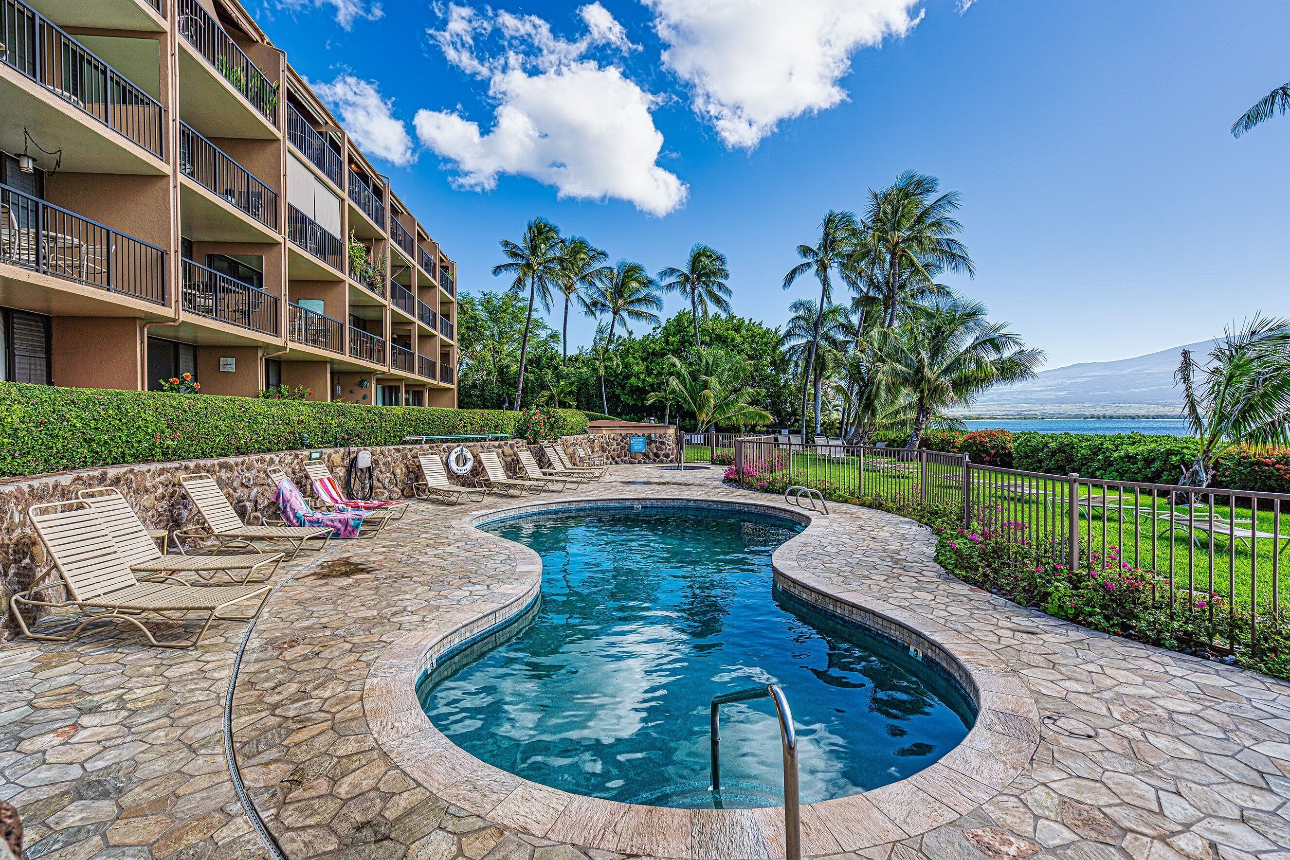 A swimming pool with lounge chairs, a stone deck, and a view of a mountain and ocean.