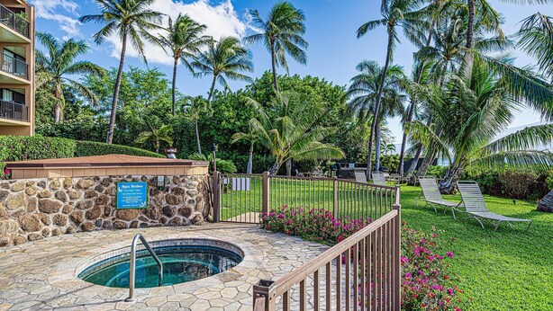 A pool area with a stone wall, a sign, and lounge chairs. - Maalaea Banyans 411 (Wailuku)