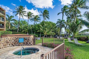 A pool area with a stone wall, a sign, and lounge chairs. - Maalaea Banyans 411 (Wailuku)