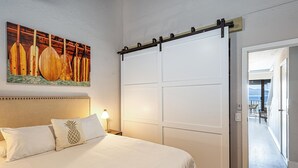 A bedroom with a bed, a sliding door, a painting of paddles, and a view of the outdoors. - Maalaea Banyans 411 (Wailuku)