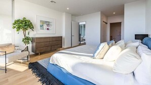A modern bedroom with a large bed, a dresser, a plant, and a framed picture on the wall. - @ Marbella Lane - Luxurious 3BR Penthouse (Long Beach)