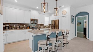 Une cuisine moderne avec des meubles blancs, un îlot central doté de tabourets, des appareils en acier inoxydable et un éclairage suspendu.
