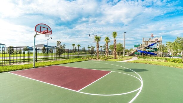 An outdoor basketball court with a green and red playing surface, surrounded by a fence, palm trees, and a water slide structure. - Pxc3151-306 (Kissimmee)