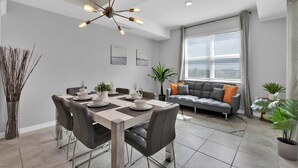 A modern dining area with a chandelier, a dining table set for four, and a grey sofa in the background. - Pxc3151-306 (Kissimmee)