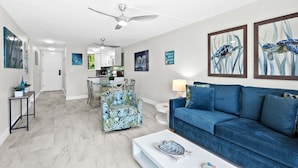 Een moderne woonkamer met een blauwe bank, een fauteuil met een patroon, en een eethoek met een witte tafel en stoelen.