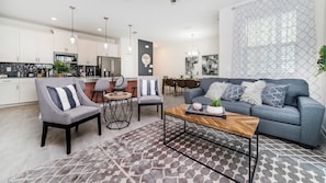 A modern living room with a grey sofa, two armchairs, a coffee table, and a dining area with a chandelier. - Wma4951 (Kissimmee)