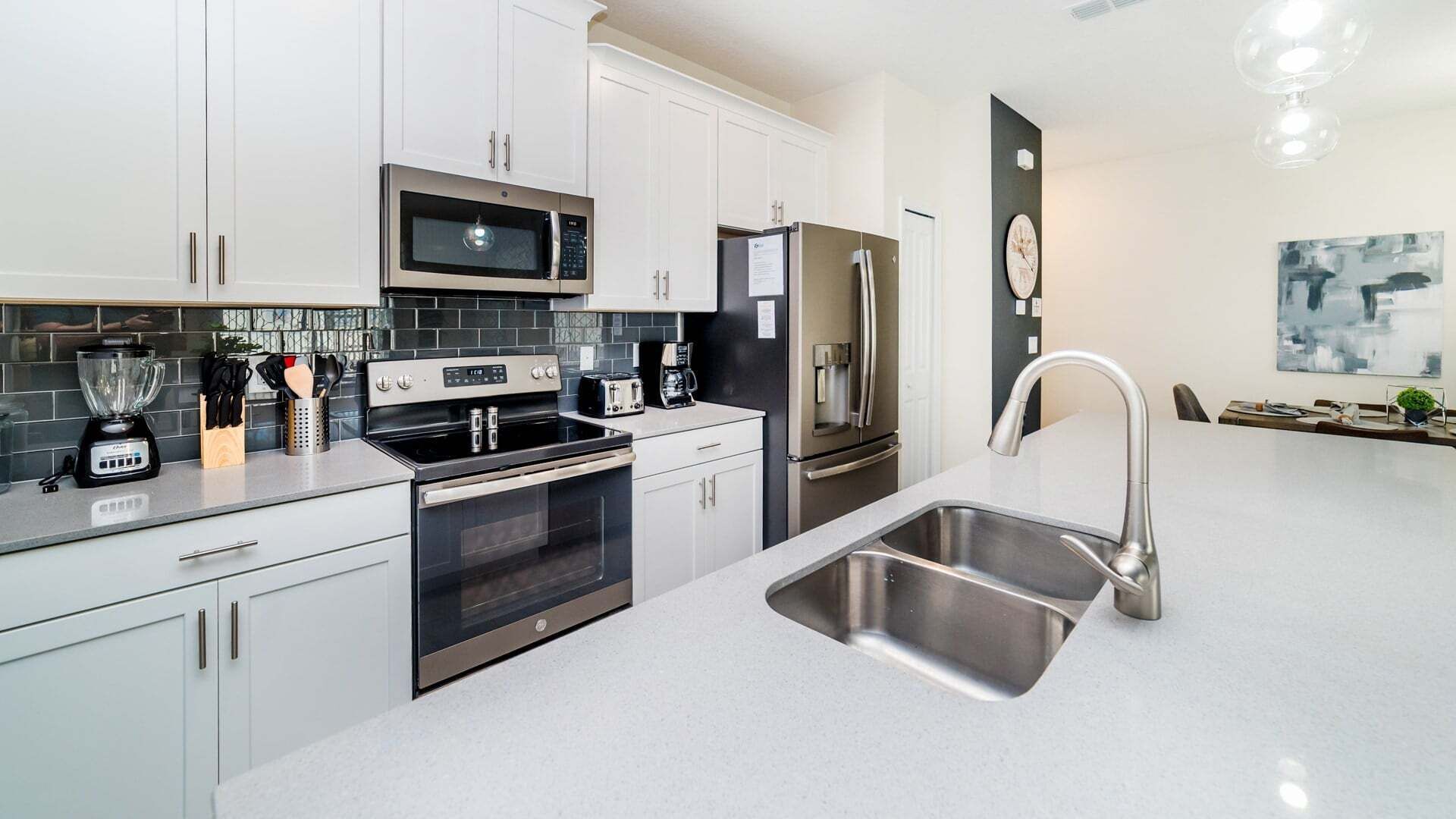 A modern kitchen with white cabinets, stainless steel appliances, a built-in oven, a microwave, a refrigerator, and a sink.