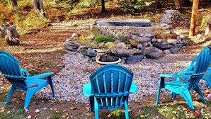 Un foyer en pierre, entouré de rochers et de feuillage, avec trois chaises bleues disposées autour.