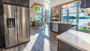 Una cocina moderna con un refrigerador de acero inoxidable, piso de madera y grandes ventanales con vista a un lago.