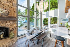 A modern kitchen with large windows, a stone fireplace, and a dining area with a bench and chairs. - Lakeside Story (Mooresville)