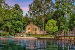 A lakeside cabin with a stone chimney, a dock, and a deck with chairs. - Lakeside Story (Mooresville)