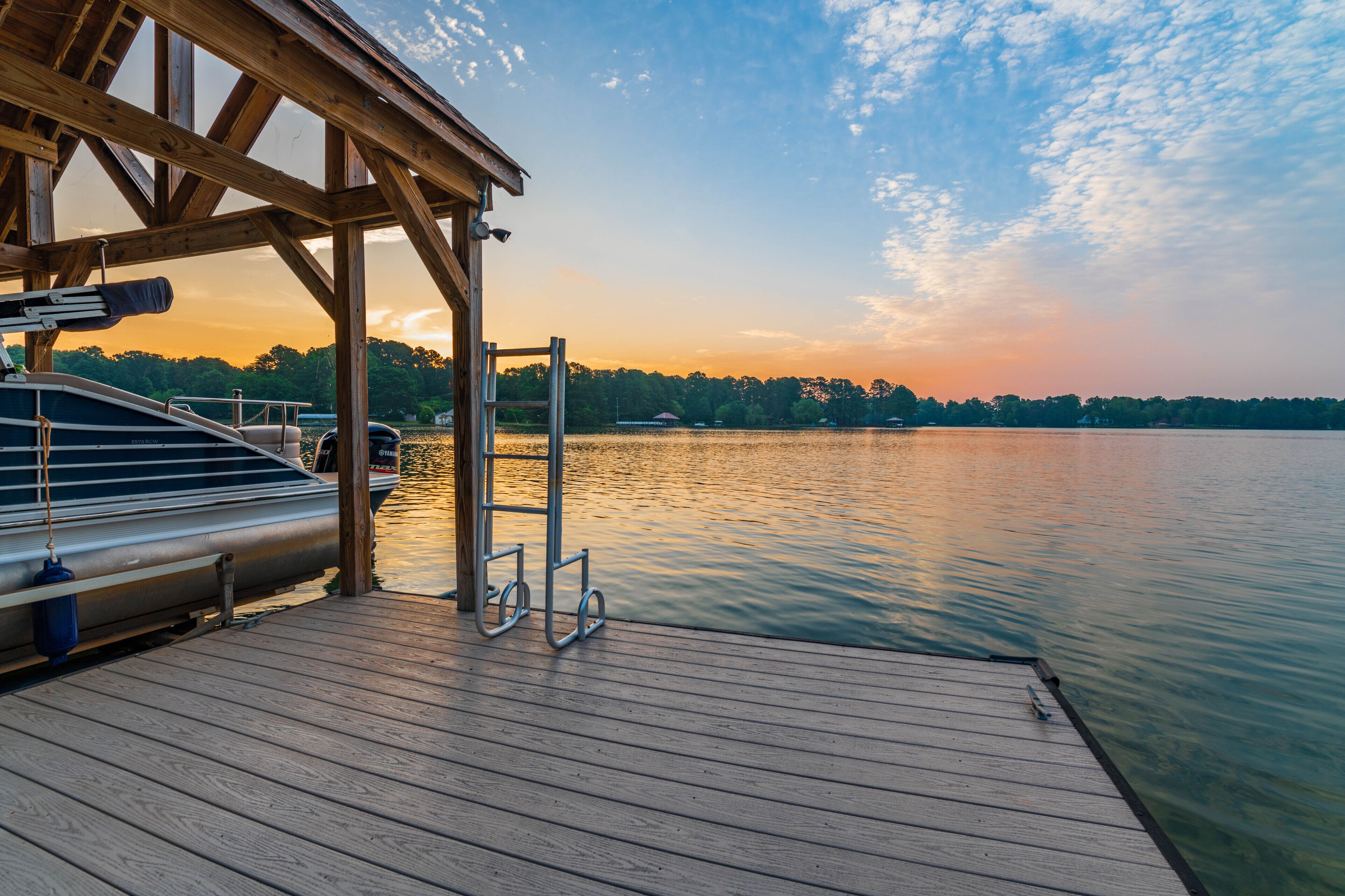 A wooden dock extending into calm water with a boat docked on the left.